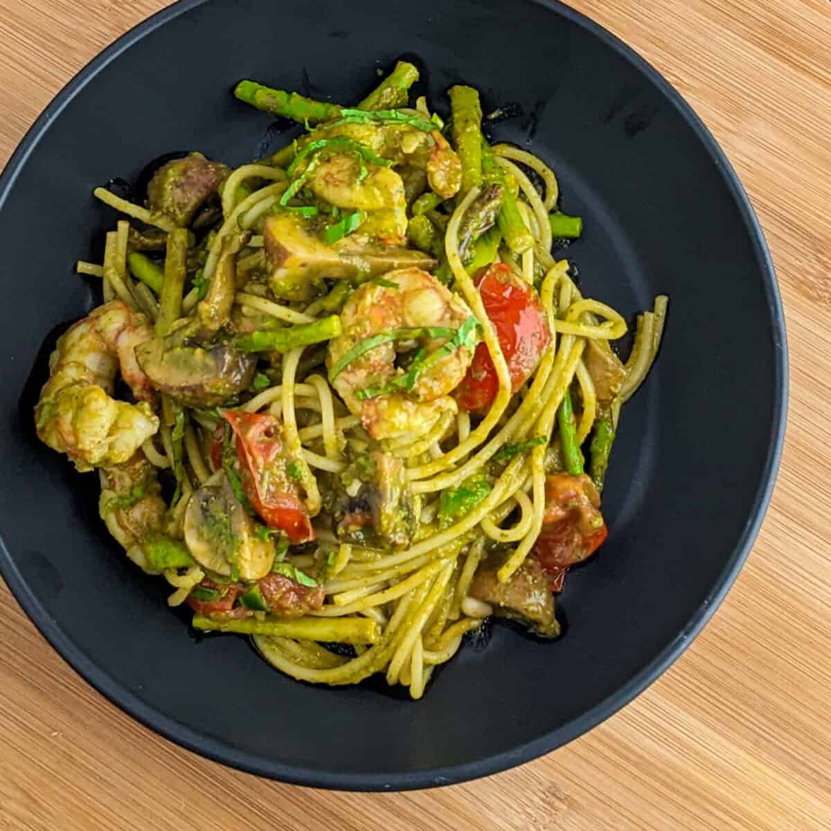 Vibrant shrimp pesto pasta with cherry tomatoes and asparagus elegantly served in a black bowl.